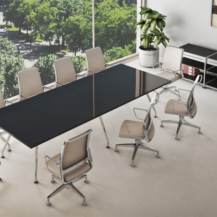The Stylus Conference Room features a sleek black rectangular table surrounded by beige swivel chairs, with expansive windows offering views of lush green trees. A potted plant adds a touch of nature, while wall shelves lined with books and files provide both function and charm. Studio Office Cyprus