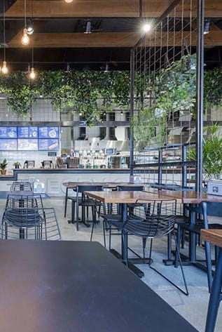 Stylish restaurants interior featuring wood tables, metal chairs, and lush greenery.