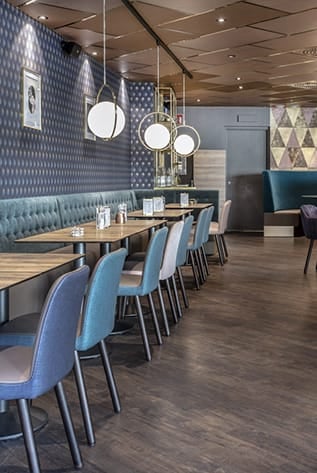 Stylish cafeterias with blue chairs, wood tables, and globe lighting. Durable furniture solutions for hospitality.