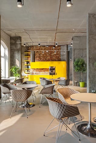 Modern cafeterias with stylish chairs, round tables, and a bright yellow counter.