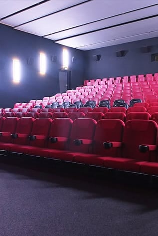 Rows of plush red Cinema seats with cup holders in a modern theater.
