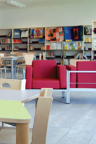 Modern library furniture: red chairs, light wood tables, and bookshelves.