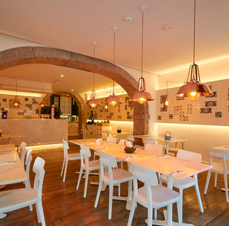 Bright, inviting Restaurants interior with white furniture, wood floors, and copper pendant lights.