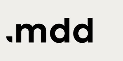 Λογότυπο MDD. Μαύρο κείμενο σε ανοιχτόχρωμο φόντο.