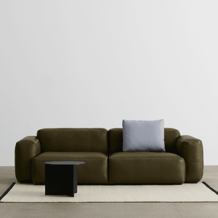 Λαδί καναπές Mags Soft Low Armrest με γαλάζιο μαξιλάρι και μαύρο βοηθητικό τραπεζάκι πάνω σε λευκό χαλί.