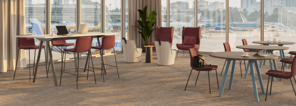 Σύγχρονος χώρος με κόκκινα σκαμπό NaughtOne Viv Stool, τραπέζια και καρέκλες σε φωτεινό, ανοιχτό σαλόνι αεροδρομίου.