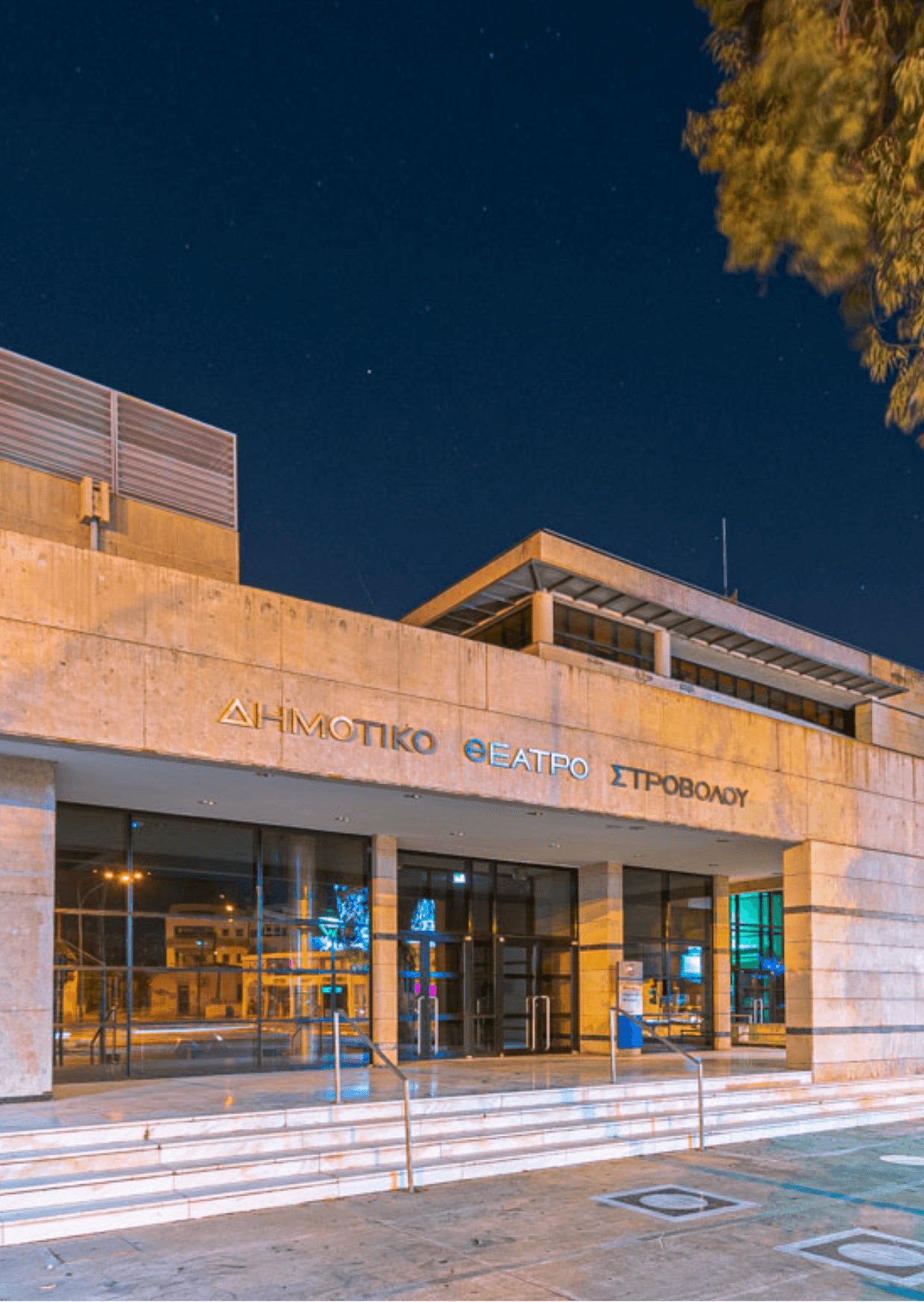 Το Δημοτικό Θέατρο Στροβόλου στο Πανεπιστήμιο Κύπρου. Σύγχρονη αρχιτεκτονική κάτω από έναστρο νυχτερινό ουρανό. Είσοδος κτιρίου με γυάλινες πόρτες.