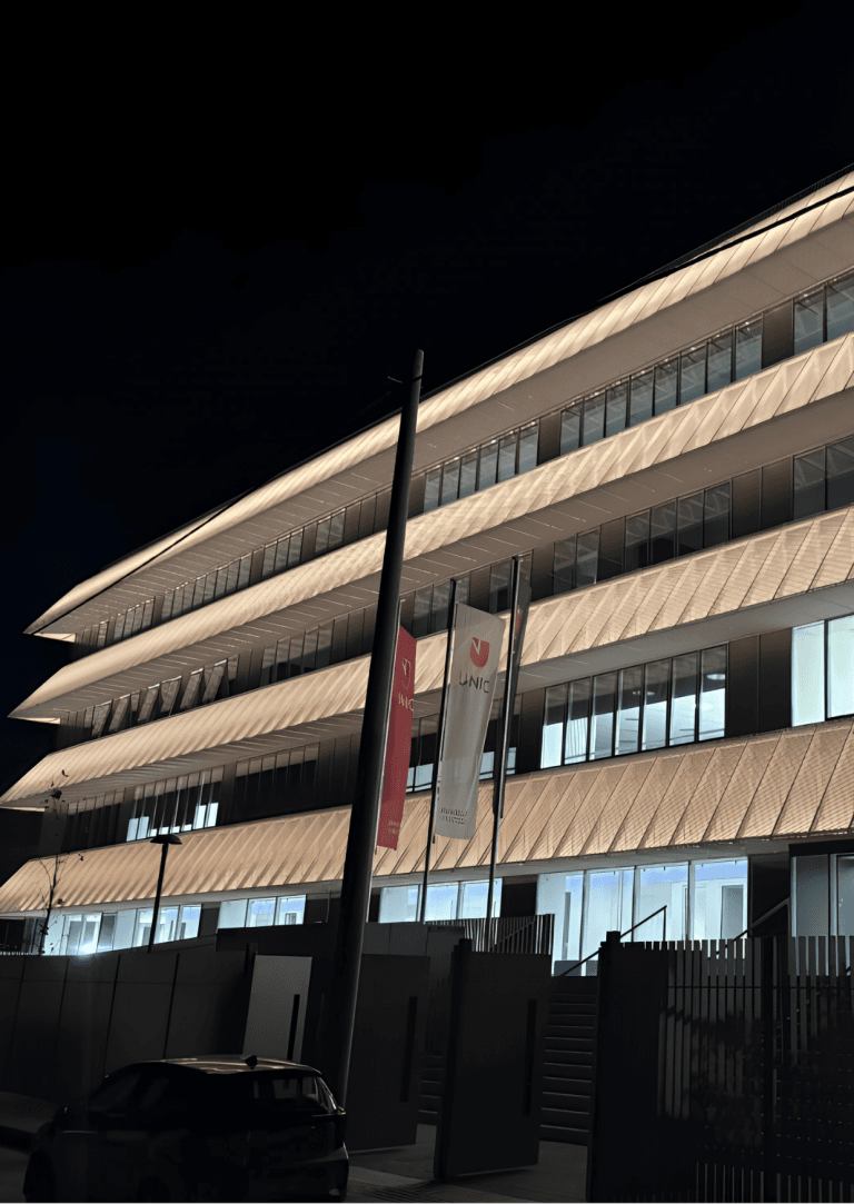 Το κτίριο του UNIC Athens Campus τη νύχτα, με φωτισμένη πρόσοψη και σημαίες του UNIC.