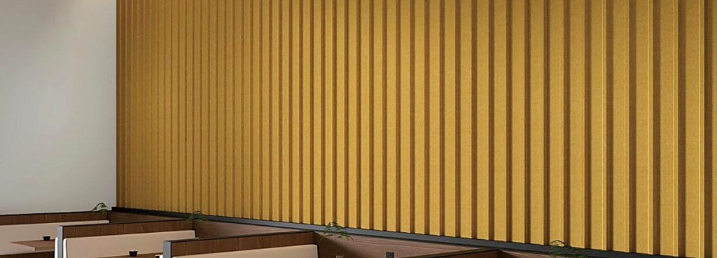 Ηχοαπορροφητικό πάνελ 3D U-Channel σε κίτρινο μουσταρδί με βαθιές κάθετες ραβδώσεις, τοποθετημένο σε τοίχο πάνω από πάγκο-καναπέ.