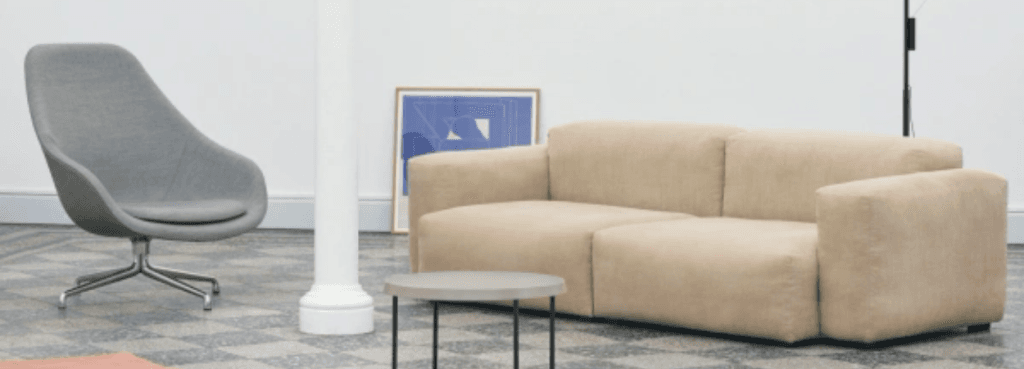 Γκρι πολυθρόνα AAL 83 Soft με μεταλλική περιστρεφόμενη βάση, δίπλα σε μπεζ καναπέ σε σύγχρονο εσωτερικό χώρο.