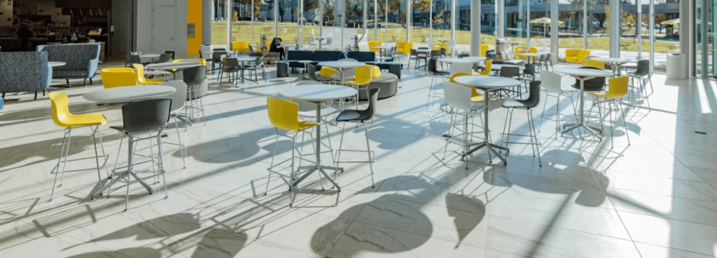 Συλλογή Bertoia Stool με κίτρινα και γκρι ανατομικά κελύφη καθίσματος, γύρω από ψηλά τραπέζια σε ηλιόλουστο αίθριο.
